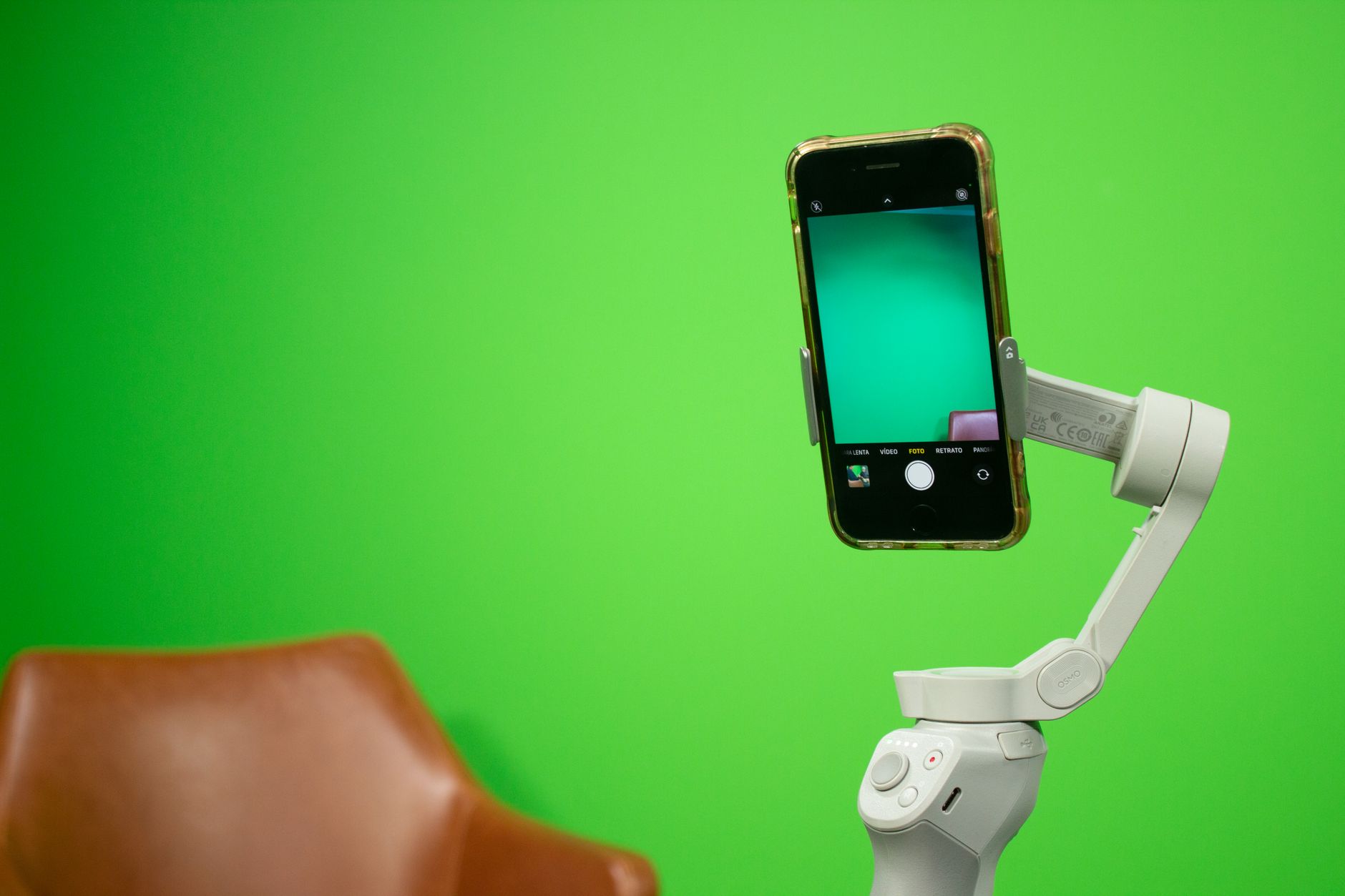 Un smartphone monté sur un stabilisateur devant un fond vert, avec l’application caméra ouverte